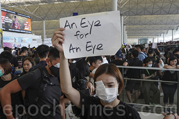 2019年8月12日，港人在香港機場展開「警察還眼」集會。圖為示威民眾舉著「以眼還眼」的標語聲援11日眼睛受傷的女性。（余鋼／大紀元）