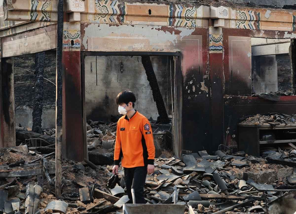 2025年3月23日,消防員撲滅了慶尚北道義城郡雲羅寺的大火,但這座古老的寺廟幾近焚燬。圖為一名緊急救援人員在廢墟中行走。(YONHAP/AFP)