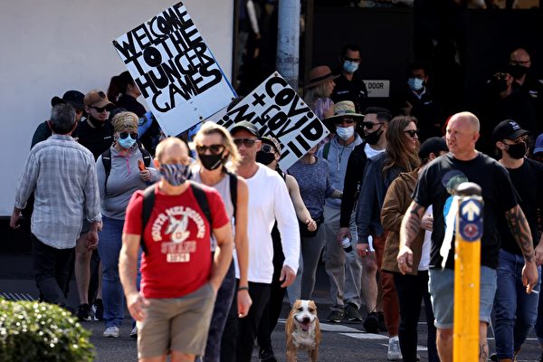 8月21日（周六），悉尼爆發反封鎖遊行。圖為抗議者舉著牌子，上面寫著「歡迎來到飢餓遊戲」、「政府+疫情=神經病」。（DAVID GRAY/AFP via Getty Images）