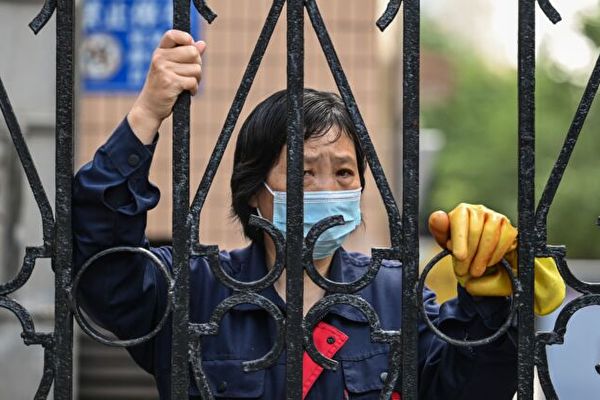  2022年5月25日，中國上海靜安區COVID-19疫情封鎖期間，一名婦女從一個大院的柵欄向外眺望。（Hector Retamal/AFP via Getty Images）