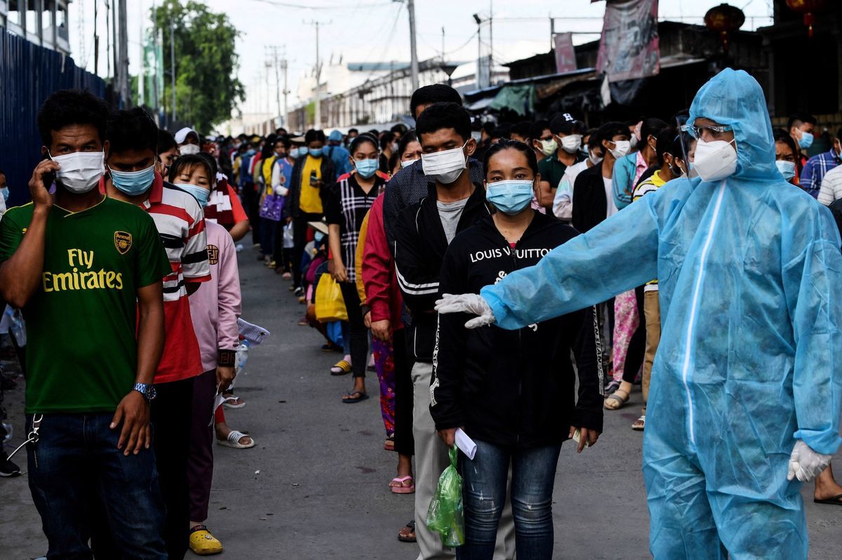 2021年5月31日，柬埔寨金邊人們排隊接種疫苗時，一名身穿防護裝備的人員，要人們保持距離。（TANG CHHIN SOTHY/AFP via Getty Images）