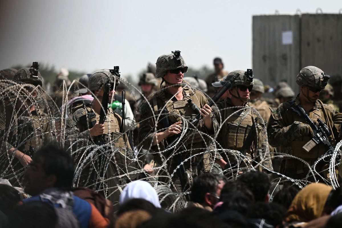 2021年8月20日，美國士兵在鐵絲網後面站崗，阿富汗人坐在喀布爾機場軍管區附近的路邊，希望在塔利班軍事接管阿富汗後逃離該國。（WAKIL KOHSAR/AFP via Getty Images）
