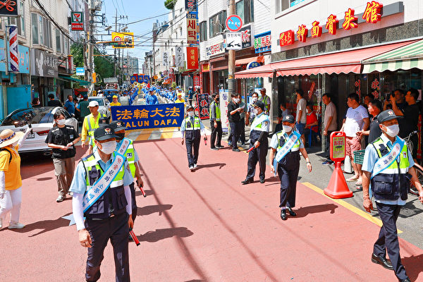 遊行隊伍經過南韓首爾中國人聚居地，南韓警察及警察助理在前方開道。（金國煥／大紀元）