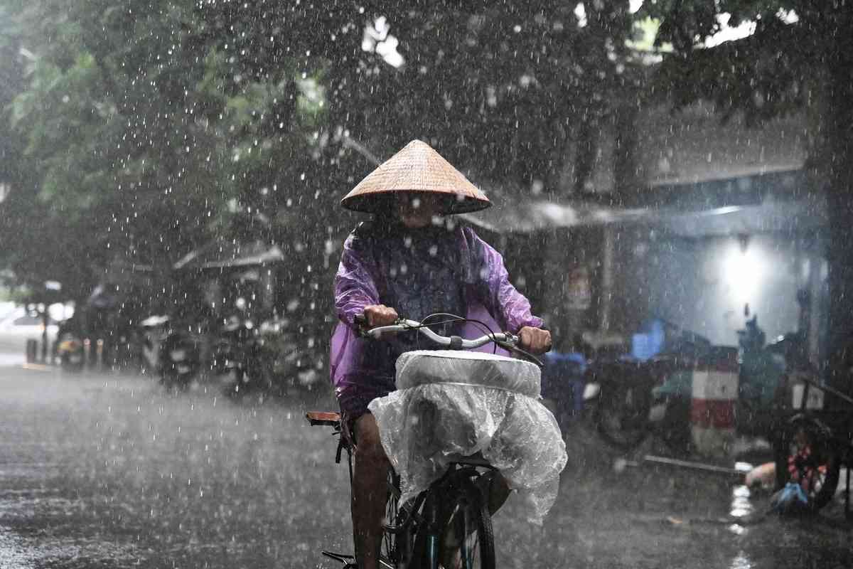 2025年10月7日,受颱風「麥德姆」(Matmo)的外圍環流影響,越南首都河內出現大範圍降雨。圖為一名婦女冒雨騎行。(Nhac Nguyen/AFP via Getty Images)