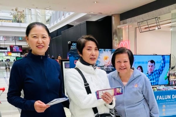 一位來自香港的女士(中)在Box Hill North Central商場法輪功展位前,開心地與義工合照。(主辦方提供)