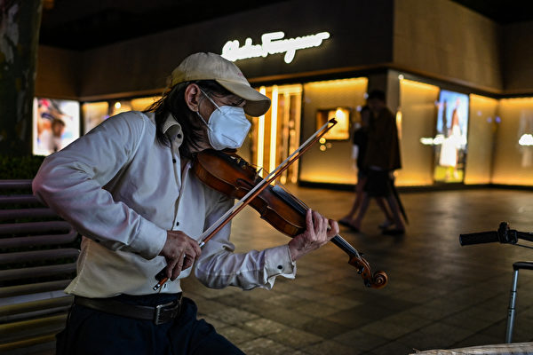 2022年6月12日，中國上海市靜安區，COVID-19（新冠病毒）疫情升溫，街上一名小提琴的演奏者戴著口罩。（Hector Retamal/AFP）