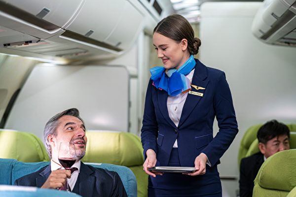 空服員提供紅酒給一名男性乘客。（Shutterstock）