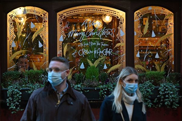 2021年12月21日，在英國倫敦，戴著口罩以防止COVID-19傳播的行人從一家酒吧的窗前走過，窗上寫著聖誕問候語。（JUSTIN TALLIS/AFP via Getty Images）