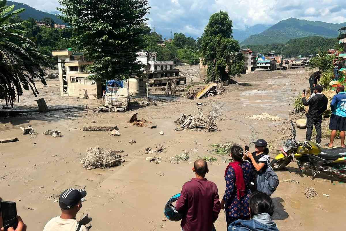 2026年8月26日，尼泊爾努瓦科特縣（Nuwakot）特里蘇里巴扎爾（Trishuli Bazar）發生山洪，河岸邊房屋部份被泥水掩埋，居民們聚在路邊觀看。（Prakash Mathema/AFP via Getty Images）