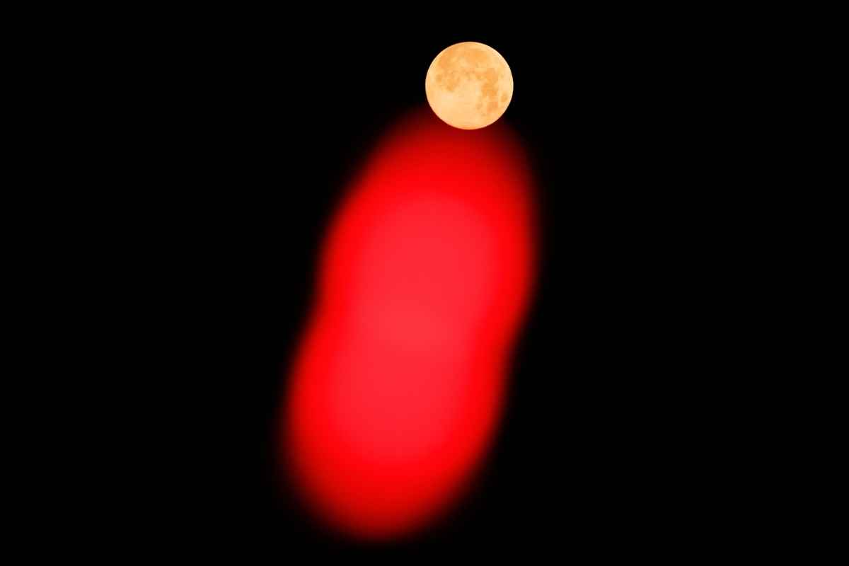 2025年1月14日日出之前,滿月高掛南韓首爾夜空,下方的紅色圖案為南韓總統尹錫悅的支持者放在總統官邸附近圍欄上的一根紅色訊號棒。(Yasuyoshi Chiba/AFP via Getty Images)