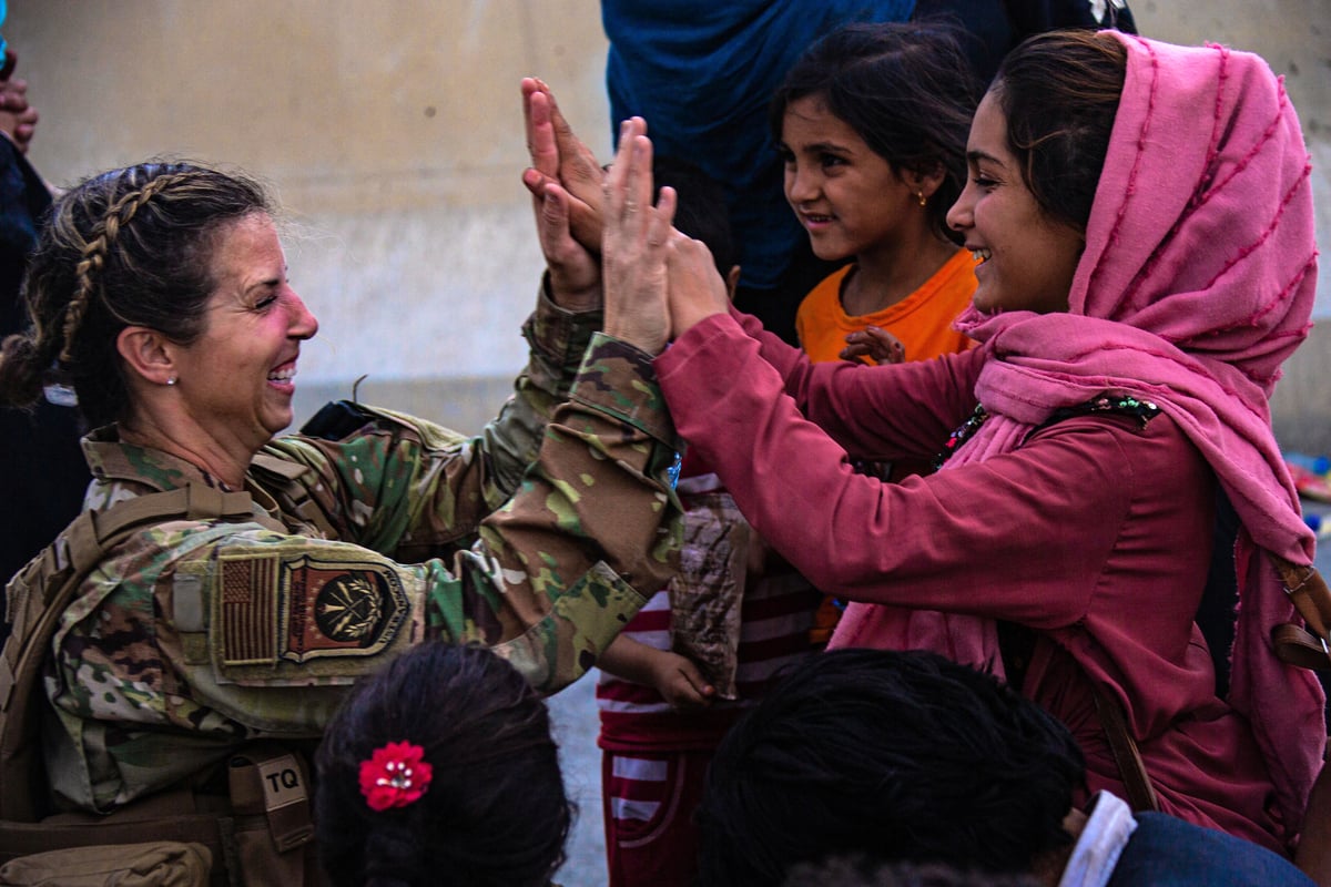 2021年8月20日，在阿富汗首都哈米德·卡爾扎伊國際機場（Hamid Karzai International Airport），危機應對聯合特遣部隊（Joint Task Force-Crisis Response）一名美國空軍女兵（左）在幫助一家人團聚後與其孩子（右）擊掌。（Davis Harris/US MARINE CORPS/AFP）
