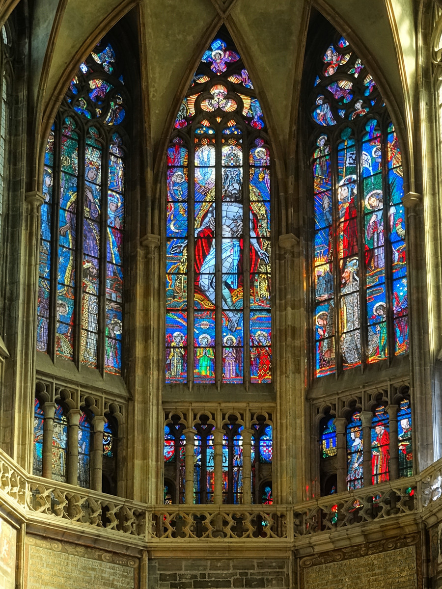 在聖維特大教堂的南側底端有三座大型玻璃花窗，組成一幅三聯畫。花窗在陽光下閃閃發光，令人心生敬畏之意。圖案的正中央為捧在天父手中的耶穌，在他們上方則有一隻白鴿，代表著基督教中三位一體的概念。在左側可以看到聖母瑪利亞，右側跪著的則為聖溫塞斯拉斯和聖維特。（ErwinMeier/CC BY-SA 4.0）