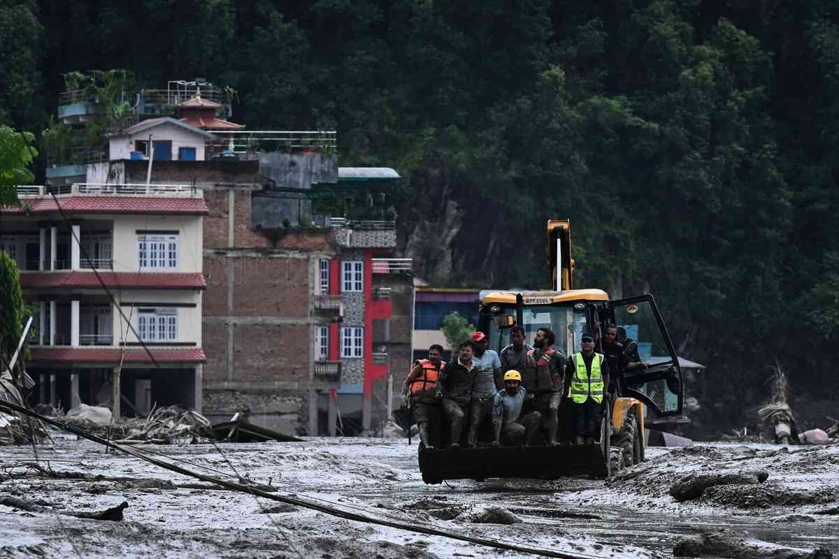 2026年8月26日，在尼泊爾努瓦科特縣（Nuwakot）德夫加特（Devghat），救援人員使用挖土機，沿著一條布滿泥水的街道運送災民及遇難者遺體。（Prakash Mathema/AFP via Getty Images）