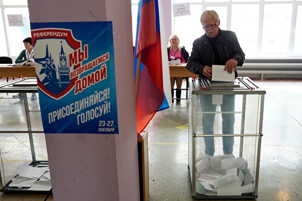 2022年9月27日，一名男子在馬里烏波爾的一個投票站投下選票。標語牌上寫著：「公投。我們正在返回家園。加入！投票！」西方國家拒絕承認這些公投，並認為其結果是俄羅斯吞併烏克蘭四個地區的藉口。（STRINGER/AFP via Getty Images）