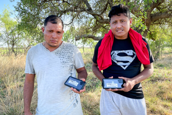 2022年4月29日，在德薩斯州金尼縣（Kinney County），兩名非法入境的尼加拉瓜公民，在被釋放到美國境內之前，舉著邊境巡邏隊發給他們的、帶有登記號碼的手機。（Charlotte Cuthbertson/The Epoch Times）