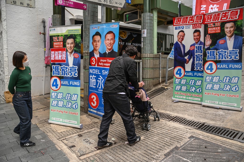 圖為2023年12月8日，行人走過香港區議會選舉的競選海報。（Peter Parks / AFP）