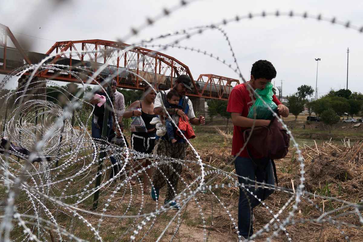 圖為2022年5月22日，穿越Rio Grande河的非法移民在德州Eagle Pass沿鐵絲網行走。（ALLISON DINNER/AFP via Getty Images）