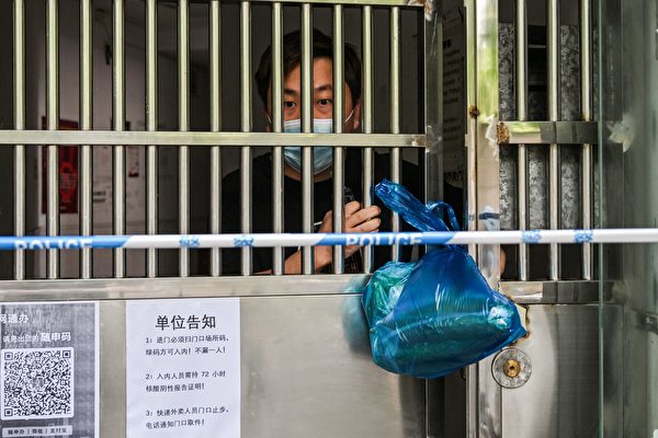 2022年6月2日，一名男子在上海靜安區被COVID-19封鎖的小區門口從一名送貨員手中接過蔬菜。（Hector Retamal/AFP via Getty Images）