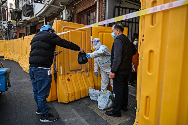 上海靜安區，一名身穿防護裝備的工人守衛著一個處於封鎖狀態的社區入口，從一名送貨員手裏接收食物。攝於2022年3月29日。（Hector Retamal/AFP via Getty Images）