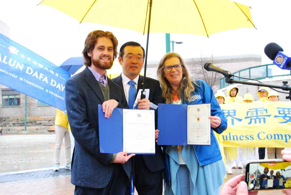 2025年5月1日,安省司法廳長道格·唐尼(Doug Downey )助理黑爾(Hale)(左)、安省簡化繁文縟節廳長、安省議員安德利亞·汗金(Andrea Khanjin)的助理黛布(Deb)(右)手持褒獎函和活動組織者張丕興合照留念,慶祝世界法輪大法日。(伊鈴/大紀元)