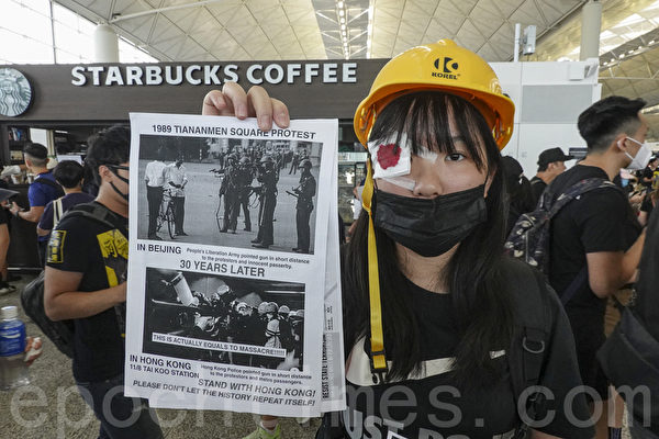 2019年8月12日，港人在香港機場展開「警察還眼」集會。圖為一位女子將1989年北京天安門廣場和30年後香港太古廣場相比較的英文海報展示給民眾。（余鋼／大紀元）