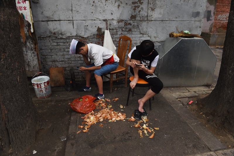 中國餐館工人在準備完蔬菜之後閱讀他們的手機。（Greg Baker/AFP）