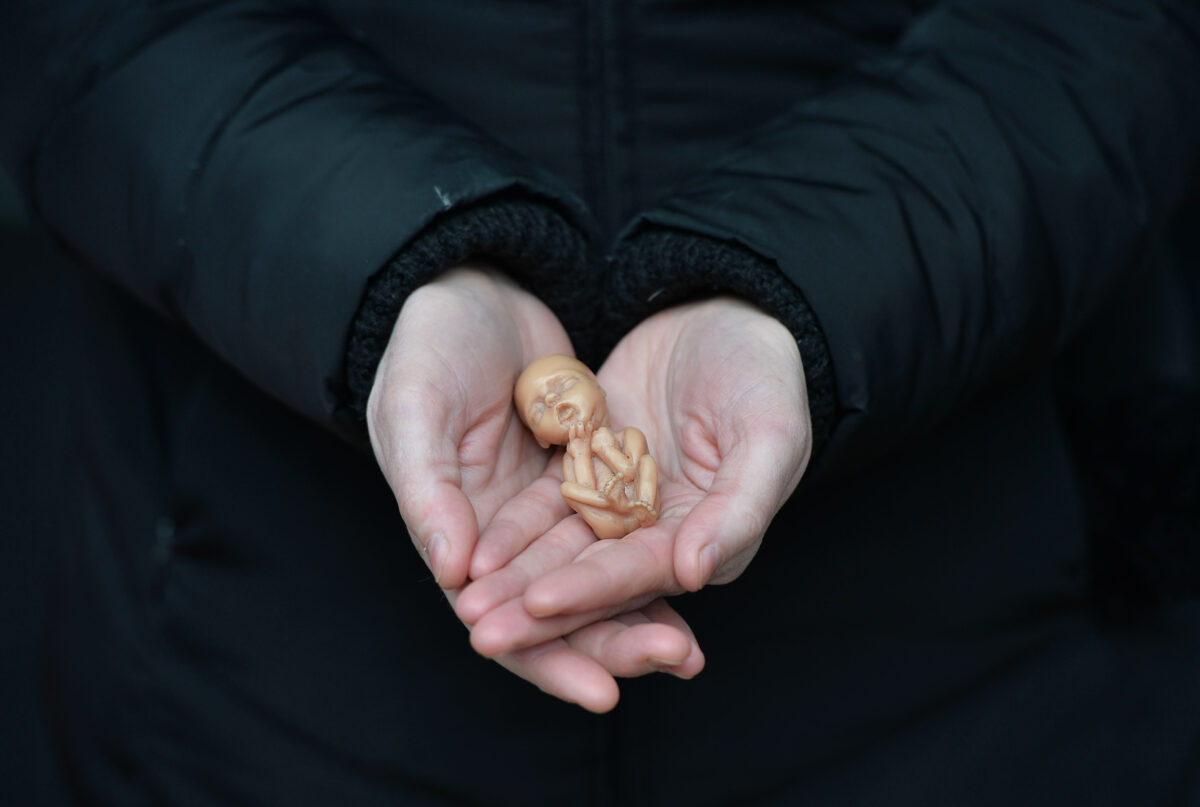 2016年4月7日，北愛爾蘭貝爾法斯特，一名反墮胎人士在瑪麗·斯特普斯診所外展示一個代表12周大的胎兒的塑料娃娃。（Charles McQuillan/Getty Images）