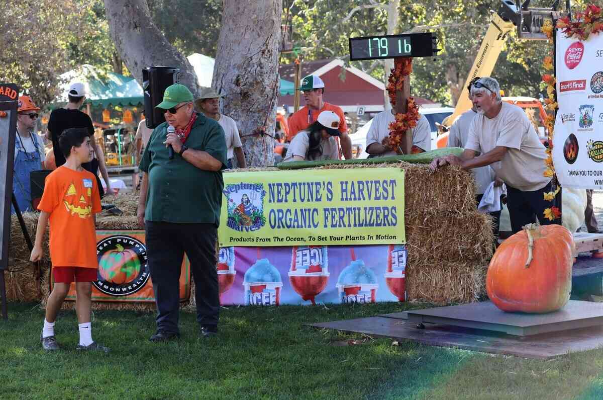 2025年9月20日,第10屆年度種植南瓜稱重大賽(Great Pumpkin Weigh-Off)在爾灣地區公園(Irvine Regional Park)舉辦。圖為來自洛縣長灘市的男孩伊恩(Ian),他種出了179磅重的南瓜,中為主持人丹尼斯(Dennis) ,右為主辦者之一史蒂夫·霍恩(Steve Horn)。(李梅/大紀元)