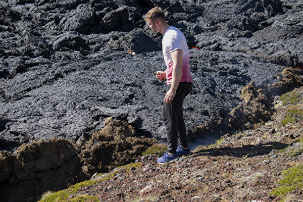 2022年8月4日，冰島法格拉達爾山（Fagradalsfjall）附近，梅拉達利爾（Meradalir）山谷的火山噴發，一名遊客將食物串在樹枝上加熱。（Jeremie Richard/AFP）