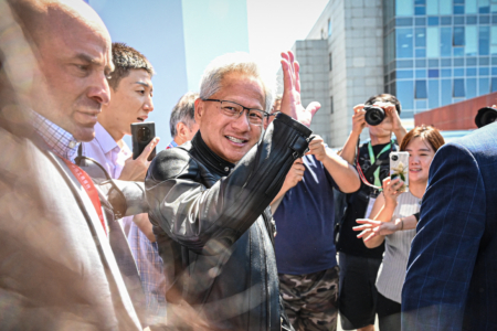 2025年7月17日,北京,中國國際供應鏈博覽會(CISCE)現場,英偉達(Nvidia)行政總裁黃仁勳(Jensen Huang,中)向現場群眾揮手致意後離場。英偉達本周獲准重啟對中國出口H20人工智能(AI)晶片,但據報該公司已告知其在中國的客戶,目前無重啟生產計劃。 (Jade Gao/AFP via Getty Images)