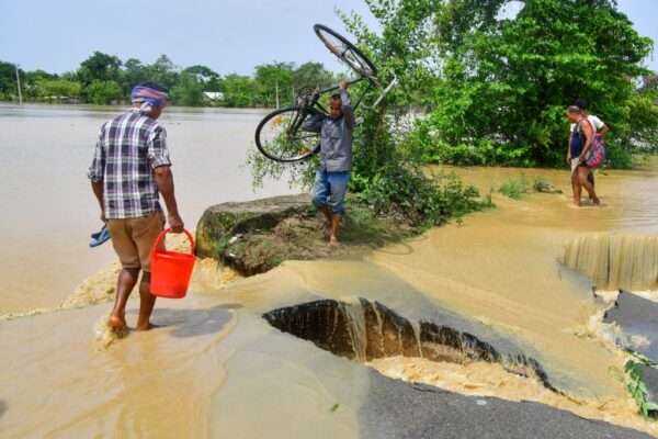 2022年5月19日，在阿薩姆邦的納貢，一名男子扛著單車穿過一條因暴雨後的洪水而被破壞的道路。（BIJU BORO/AFP via Getty Images）