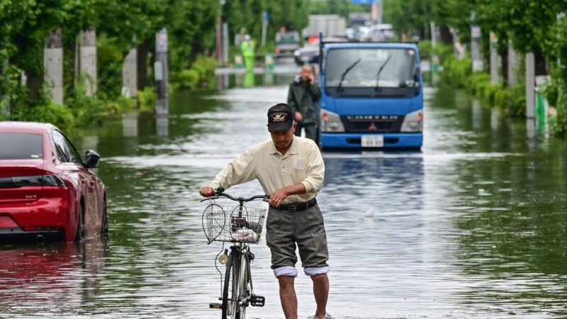 2023年6月3日，埼玉縣越谷，一名男子推著單車走在因洪水而關閉的道路上。（STR/JI Press/AFP via Getty Images）
