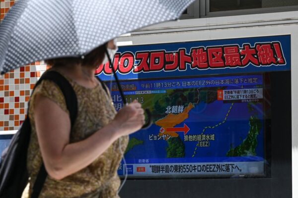 2023年7月12日，在東京市中心的一條行人路上，一名婦女一邊躲避陽光一邊走過一則有關北韓發射導彈的電視新聞報道。（RICHARD A. BROOKS/AFP via Getty Images）