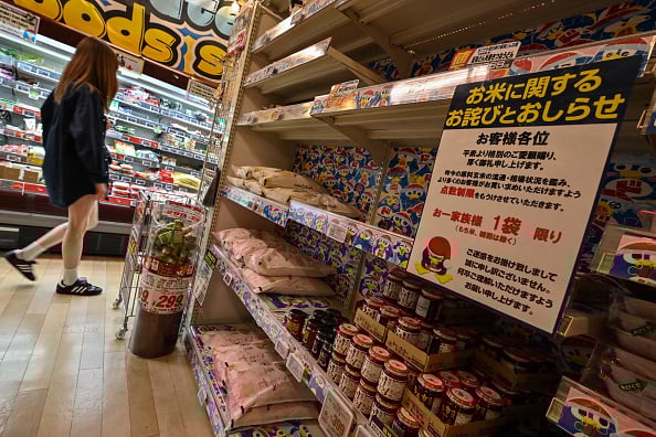 2025 年 4 月 21 日,照片中一位顧客走過大米展示台,展示台上掛著一個牌子(右),向購物者道歉,由於市場情況,每人只能購買一袋大米。(RICHARD A. BROOKS/AFP via Getty Images)